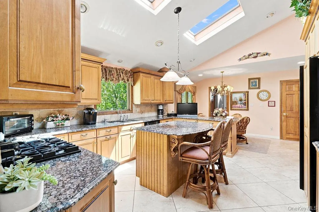 Kitchen featuring wood cabinetry, granite countertops, tile flooring, a gas cooktop, and skylights Kitchen featuring wood cabinetry, granite countertops, tile flooring, a gas cooktop, and skylights