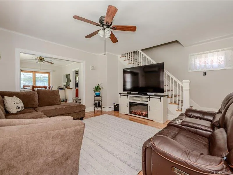 Living area featuring wood-finish flooring, light neutral wall paint, and a classic white staircase with railing Living area featuring wood-finish flooring, light neutral wall paint, and a classic white staircase with railing