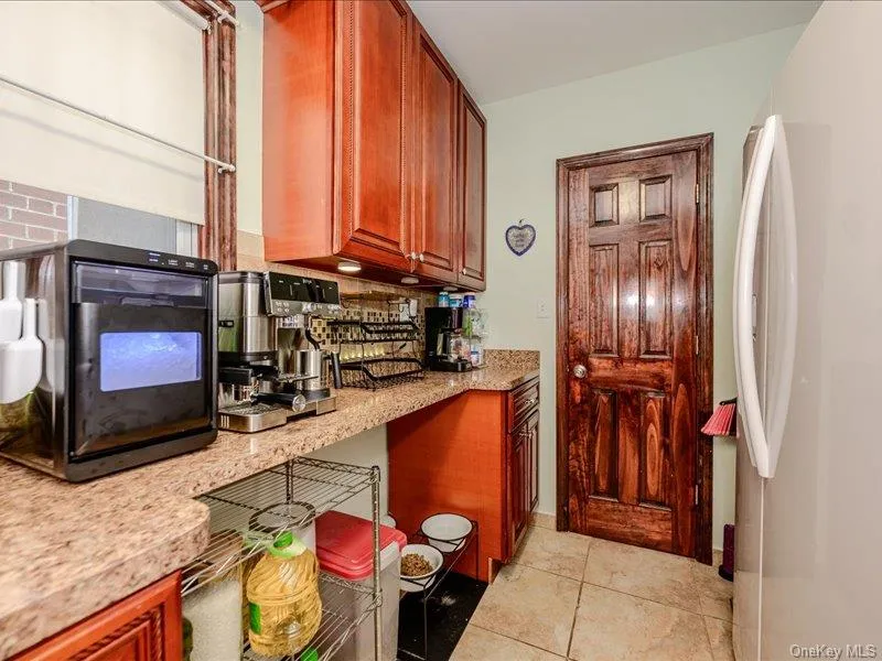 Kitchen area featuring warm-toned cabinetry, and light tile flooring Kitchen area featuring warm-toned cabinetry, and light tile flooring