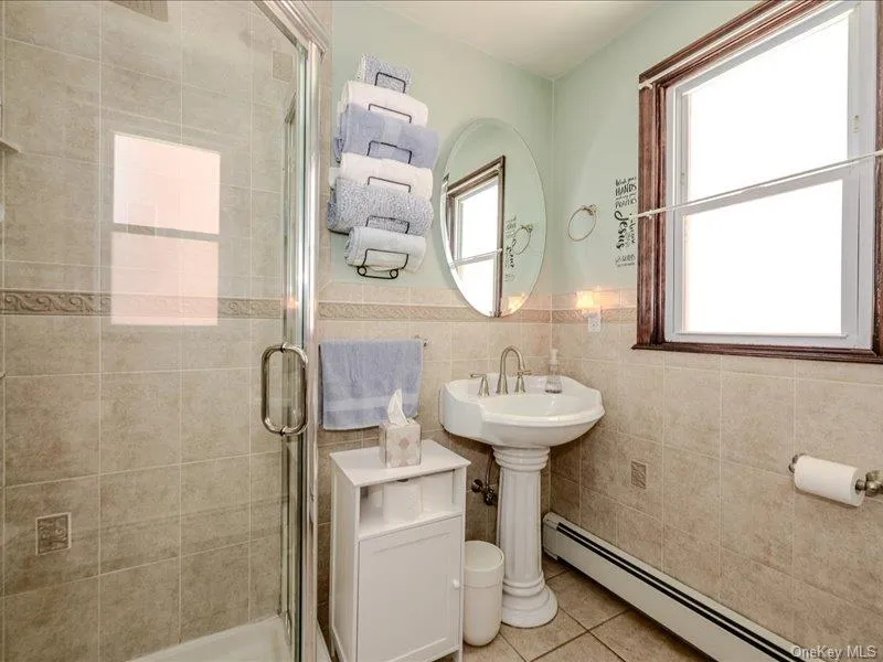 1st Floor Bathroom featuring a glass-enclosed shower, pedestal sink with a chrome faucet, and tiled walls with decorative banding 1st Floor Bathroom featuring a glass-enclosed shower, pedestal sink with a chrome faucet, and tiled walls with decorative banding
