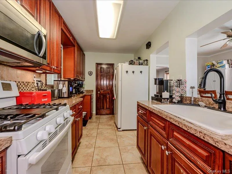 Galley kitchen featuring wood-finish cabinetry, stone-look countertops, and tile flooring Galley kitchen featuring wood-finish cabinetry, stone-look countertops, and tile flooring