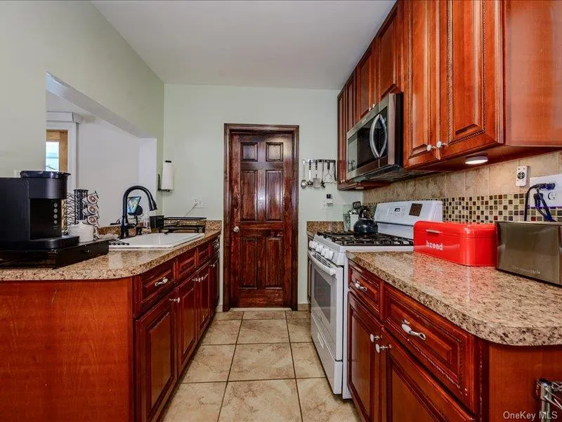 Galley kitchen featuring wood cabinetry, solid surface countertops, tile flooring, a tile backsplash, and a built-in microwave Galley kitchen featuring wood cabinetry, solid surface countertops, tile flooring, a tile backsplash, and a built-in microwave
