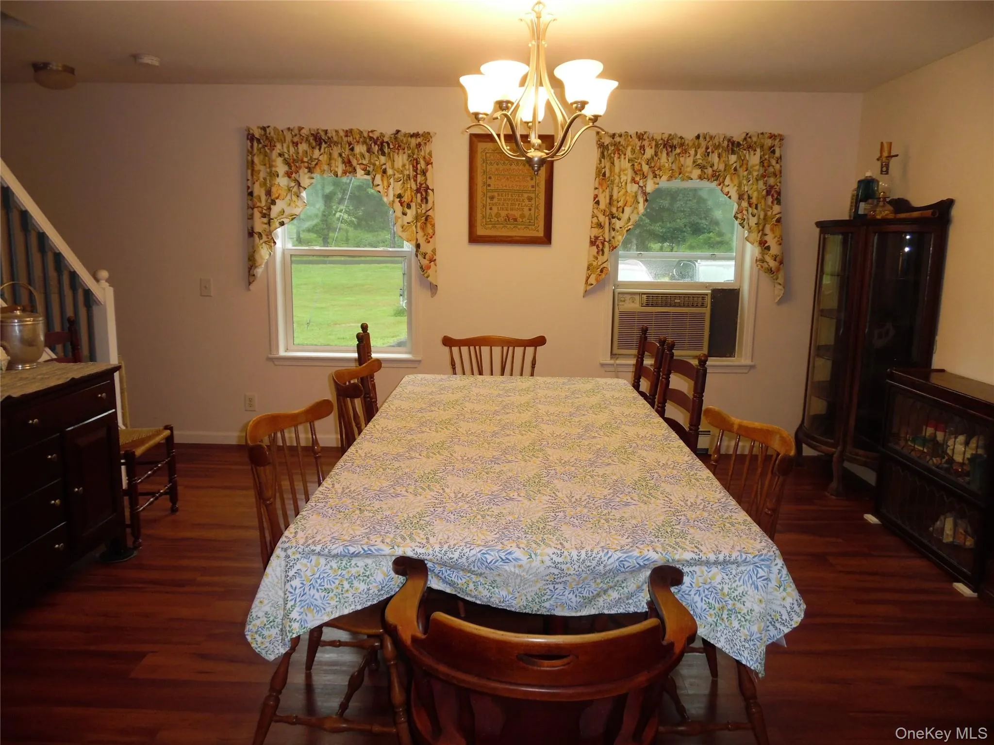 Dining area featuring wood-finish flooring, two windows with white trim, and a brass chandelier Dining area featuring wood-finish flooring, two windows with white trim, and a brass chandelier