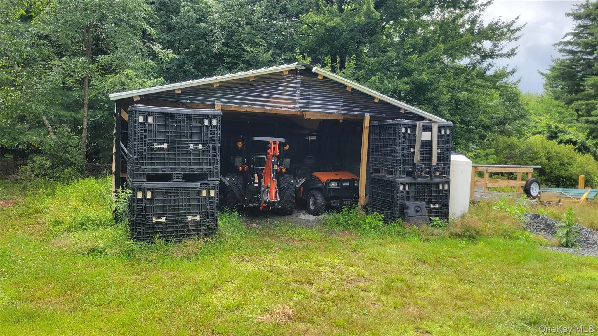 Open-sided shed with a corrugated metal roof, wood support beams, and a gravel base Open-sided shed with a corrugated metal roof, wood support beams, and a gravel base