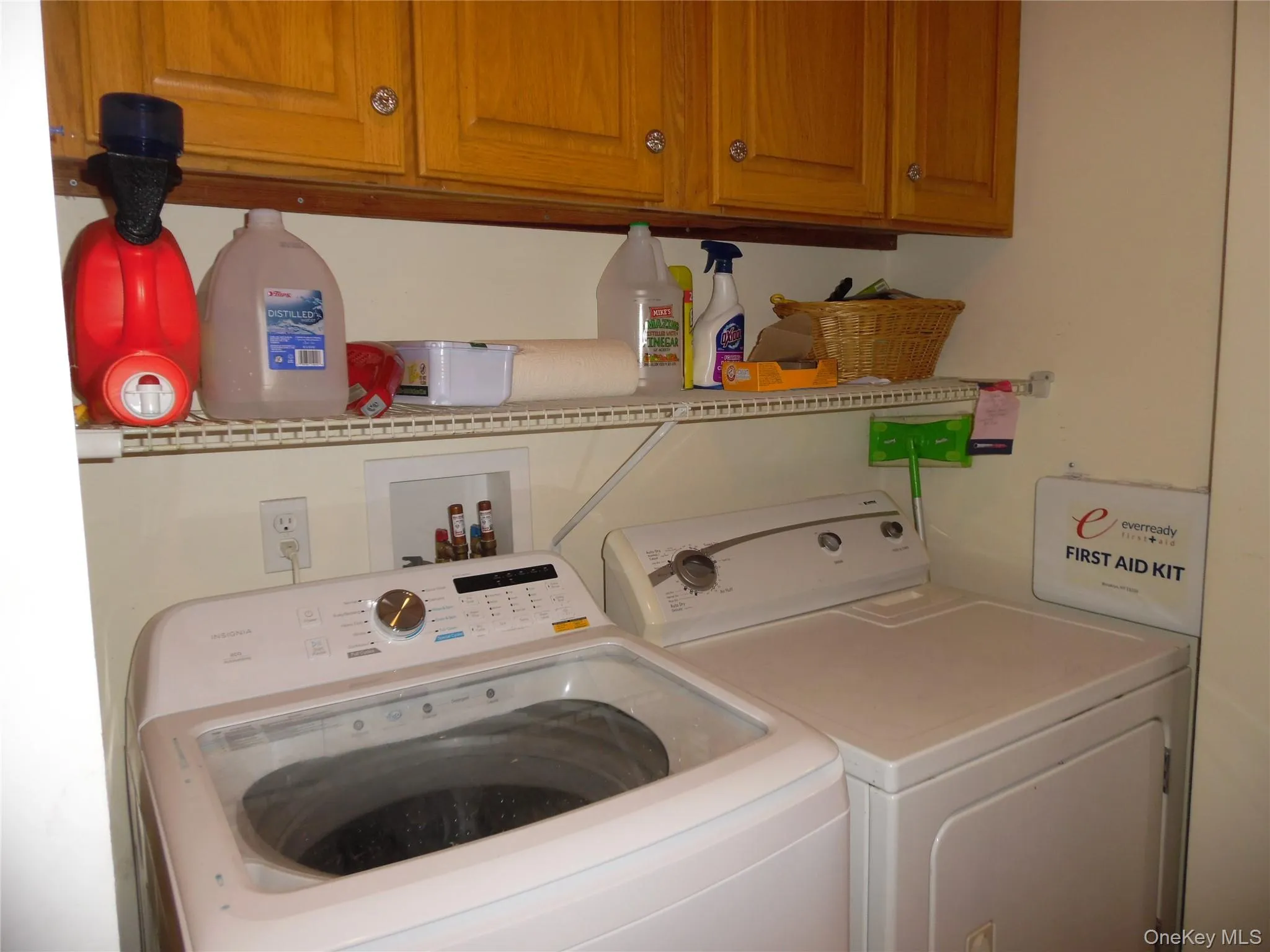 Dedicated laundry area featuring overhead wood cabinetry, a white wire shelving unit, and integrated appliance hookups Dedicated laundry area featuring overhead wood cabinetry, a white wire shelving unit, and integrated appliance hookups