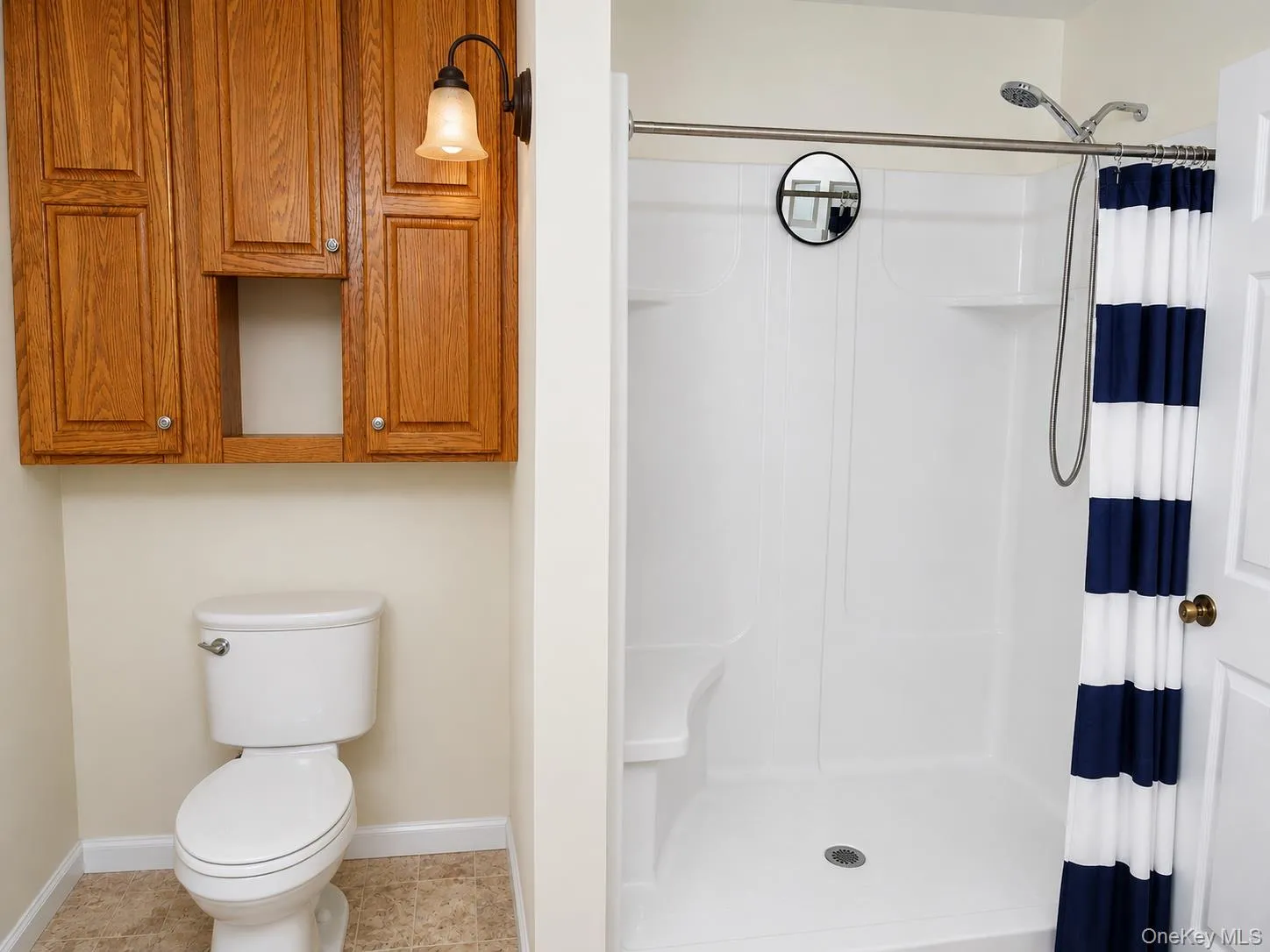 Full bathroom featuring a white toilet, wood-finish cabinetry with silver hardware, and an attached wall sconce Full bathroom featuring a white toilet, wood-finish cabinetry with silver hardware, and an attached wall sconce