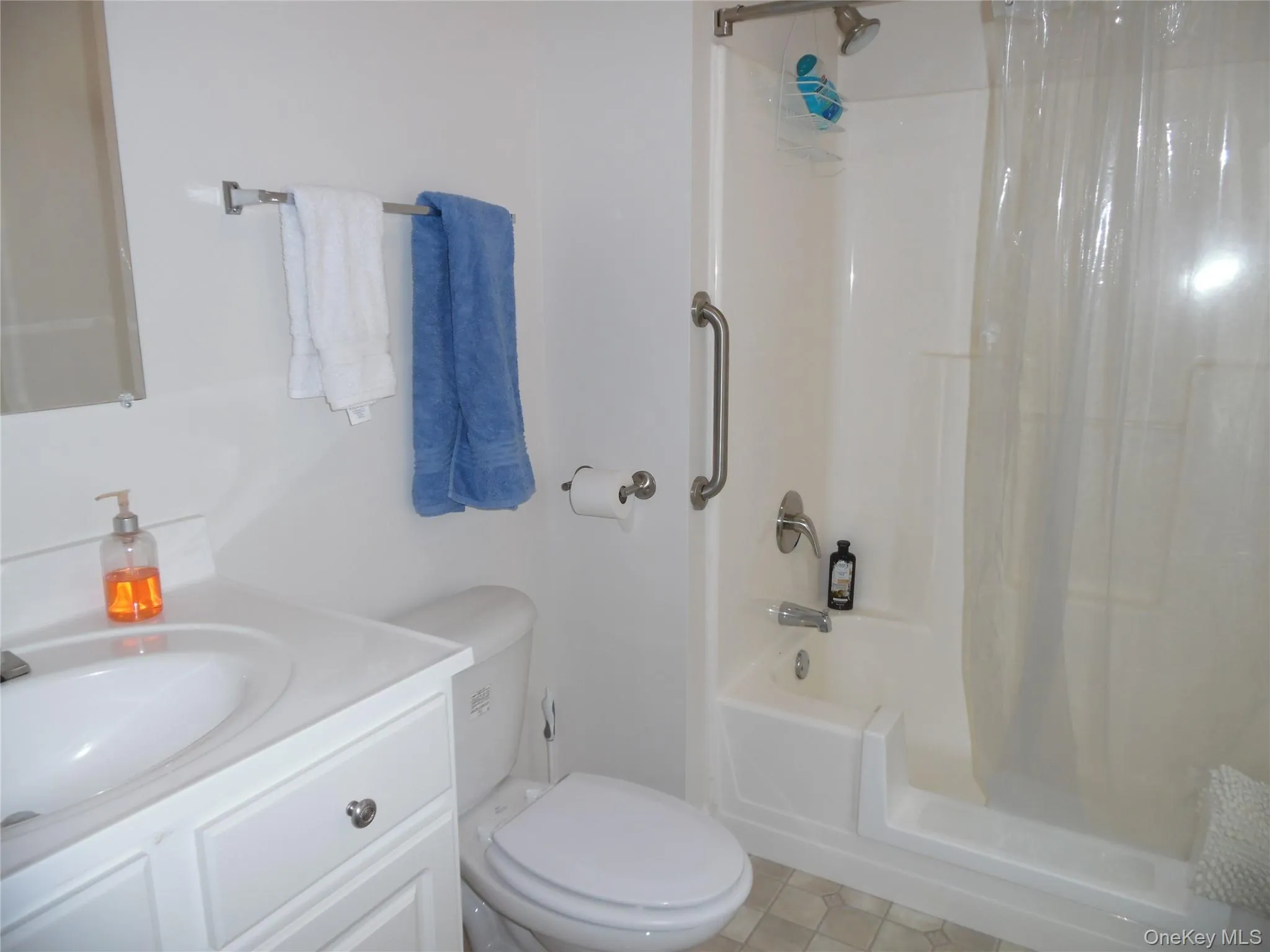 Bathroom featuring a white vanity with integrated sink, white toilet, and a white tub/shower combination with grab bar Bathroom featuring a white vanity with integrated sink, white toilet, and a white tub/shower combination with grab bar