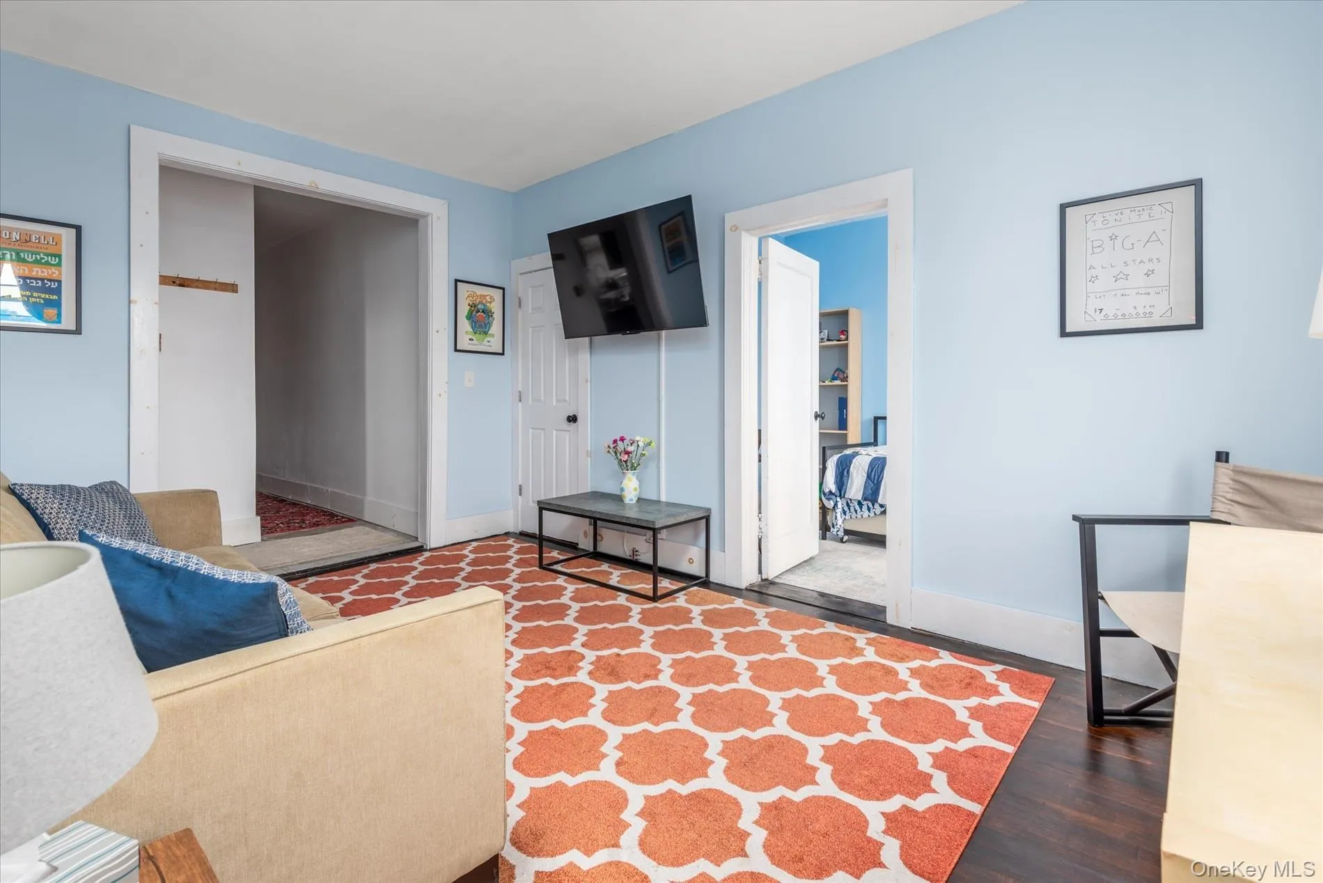 Room featuring light blue walls, dark wood-finish flooring, white trim, and a patterned area rug Room featuring light blue walls, dark wood-finish flooring, white trim, and a patterned area rug