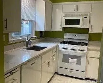 Modern kitchen featuring white cabinetry, light-toned countertops, a stainless steel sink with a gooseneck faucet, a white gas range, and a built-in microwave Modern kitchen featuring white cabinetry, light-toned countertops, a stainless steel sink with a gooseneck faucet, a white gas range, and a built-in microwave