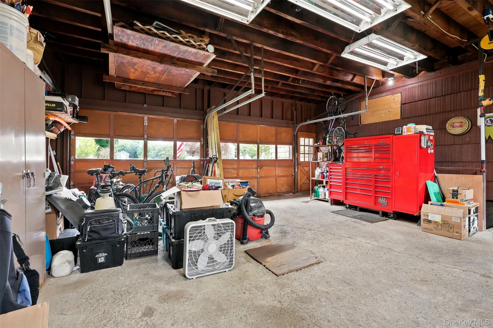 Garage with exposed wood beam ceiling, concrete flooring, and multiple fluorescent light fixtures Garage with exposed wood beam ceiling, concrete flooring, and multiple fluorescent light fixtures