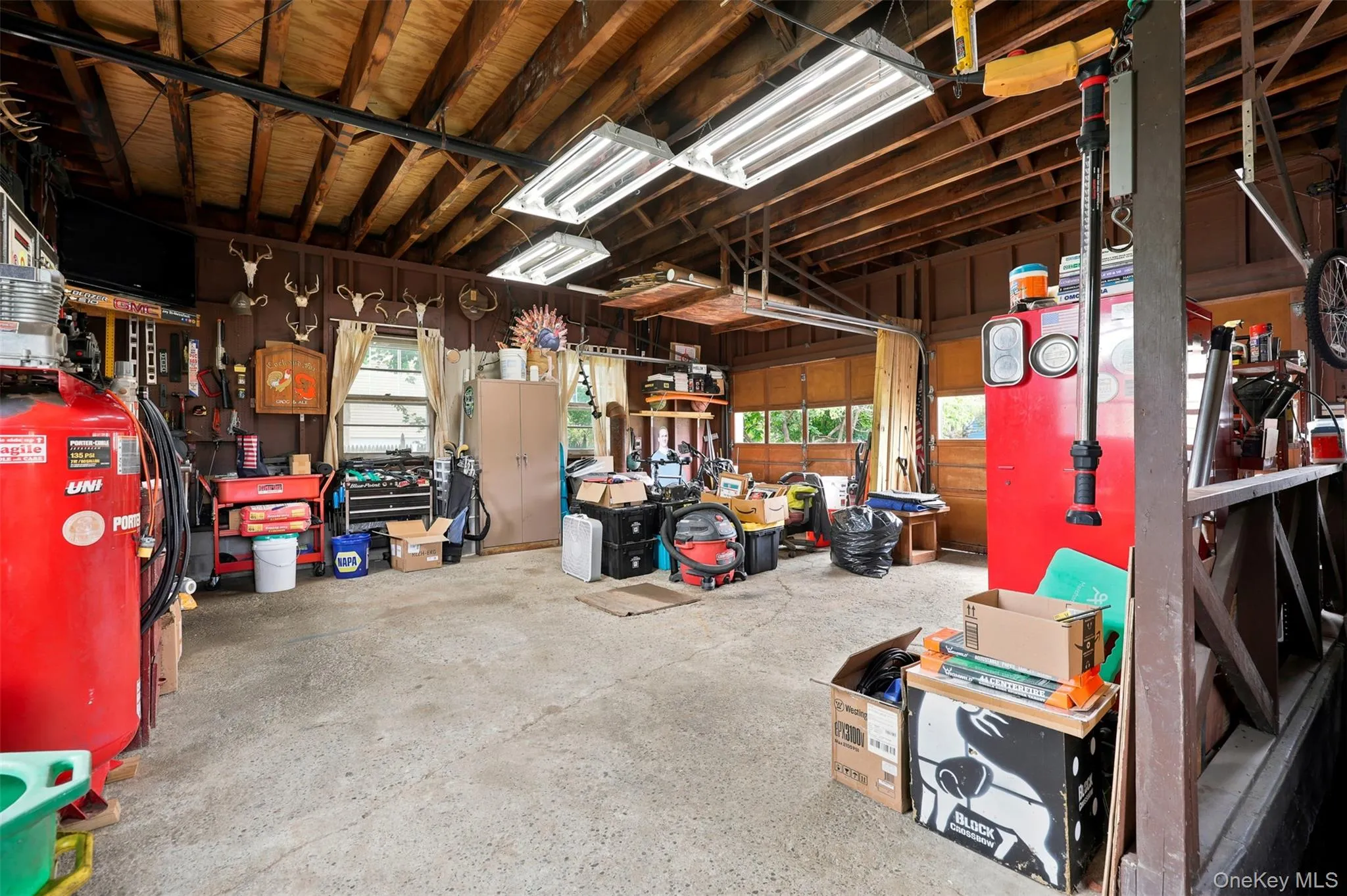 Garage with exposed wood beam ceiling, concrete flooring, and multiple fluorescent light fixtures Garage with exposed wood beam ceiling, concrete flooring, and multiple fluorescent light fixtures