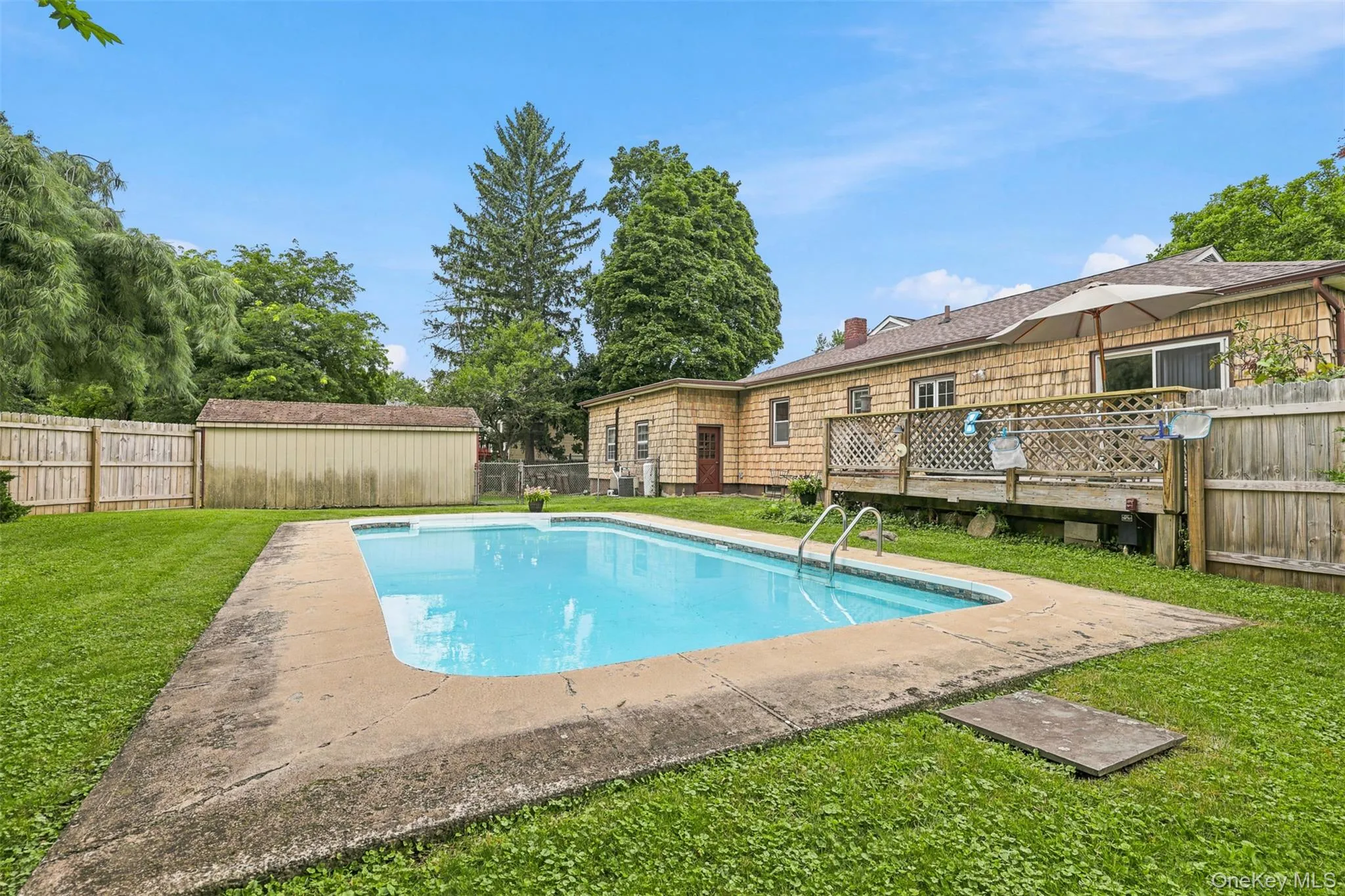 Backyard featuring an in-ground swimming pool with concrete coping, surrounded by a green lawn Backyard featuring an in-ground swimming pool with concrete coping, surrounded by a green lawn