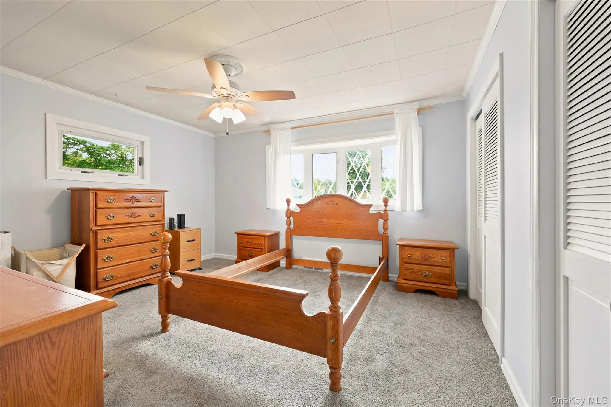 Carpeted bedroom featuring a ceiling fan, two windows, and bi-fold louvered closet doors Carpeted bedroom featuring a ceiling fan, two windows, and bi-fold louvered closet doors