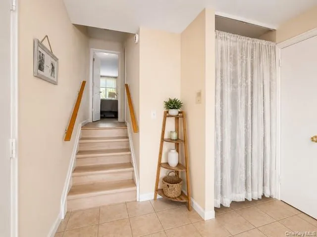 Entryway featuring neutral-toned tile flooring, a carpeted staircase with wood handrails, a white interior door, and a recessed area with a decorative curtain Entryway featuring neutral-toned tile flooring, a carpeted staircase with wood handrails, a white interior door, and a recessed area with a decorative curtain