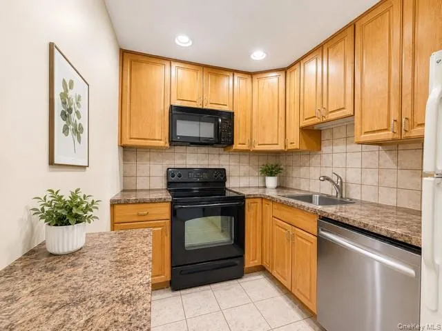 Kitchen featuring wood cabinetry, a stainless steel sink, a black electric range with an overhead microwave, and a stainless steel dishwasher Kitchen featuring wood cabinetry, a stainless steel sink, a black electric range with an overhead microwave, and a stainless steel dishwasher