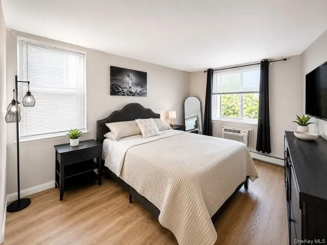 Spacious room featuring light wood-finish flooring, multiple windows with blinds, and a built-in wall air conditioning unit Spacious room featuring light wood-finish flooring, multiple windows with blinds, and a built-in wall air conditioning unit