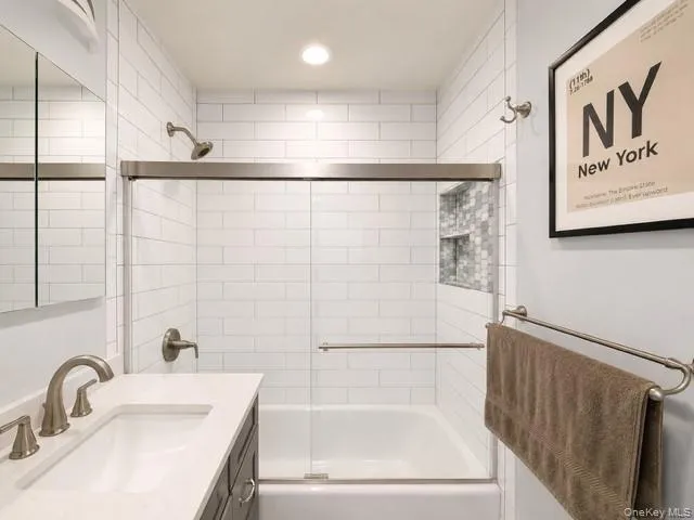 Modern bathroom featuring a tiled tub and shower combination with sliding glass doors, a built-in mosaic tile niche, and brushed nickel fixtures Modern bathroom featuring a tiled tub and shower combination with sliding glass doors, a built-in mosaic tile niche, and brushed nickel fixtures