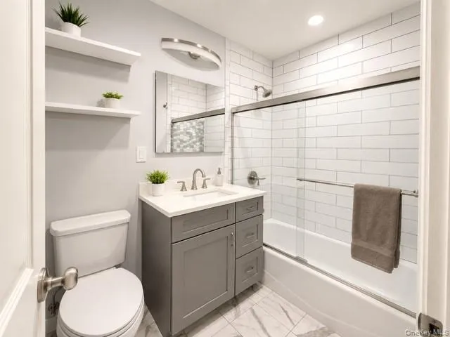 Bathroom featuring a gray vanity with white countertop, subway tile shower surround, and sliding glass shower door Bathroom featuring a gray vanity with white countertop, subway tile shower surround, and sliding glass shower door