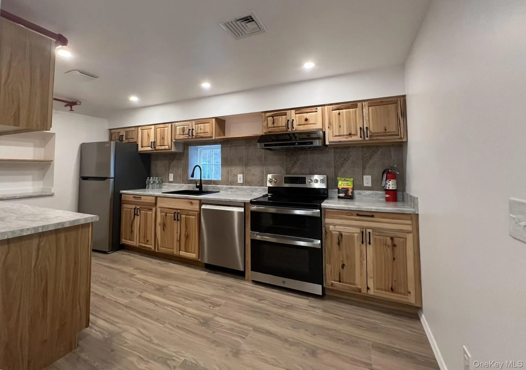 Modern kitchen featuring light wood cabinetry, stone-finish countertops, stainless steel appliances, a black sink with a gooseneck faucet, and wood-finish flooring. Modern kitchen featuring light wood cabinetry, stone-finish countertops, stainless steel appliances, a black sink with a gooseneck faucet, and wood-finish flooring.