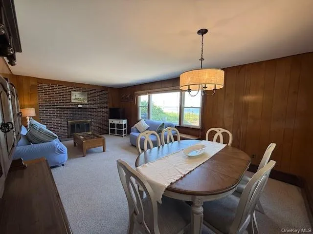 Dining area featuring light carpet, wooden walls, and a fireplace Dining area featuring light carpet, wooden walls, and a fireplace