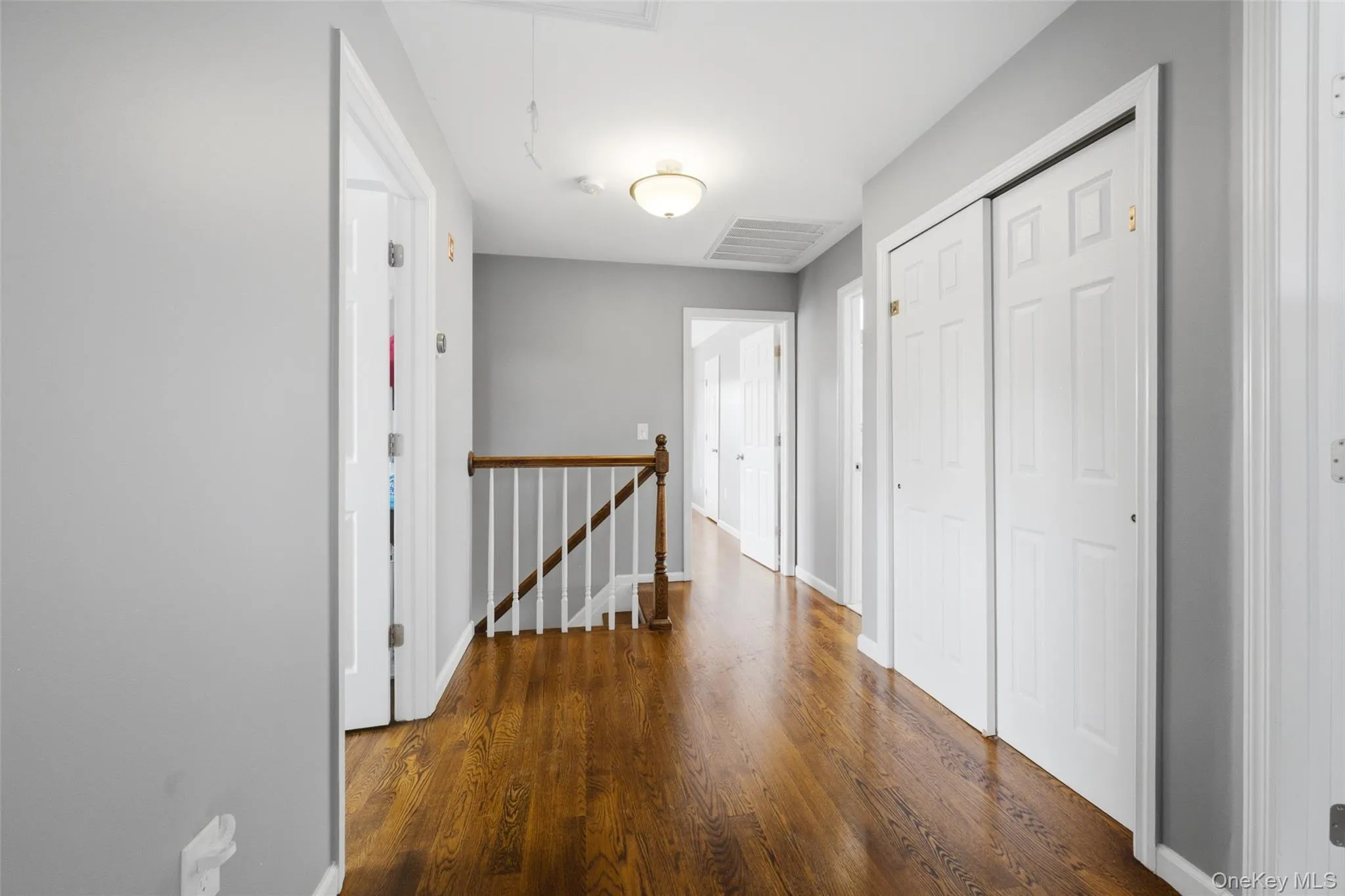 Hallway featuring wood-finish flooring, white paneled doors, and a wood railing with white spindles Hallway featuring wood-finish flooring, white paneled doors, and a wood railing with white spindles