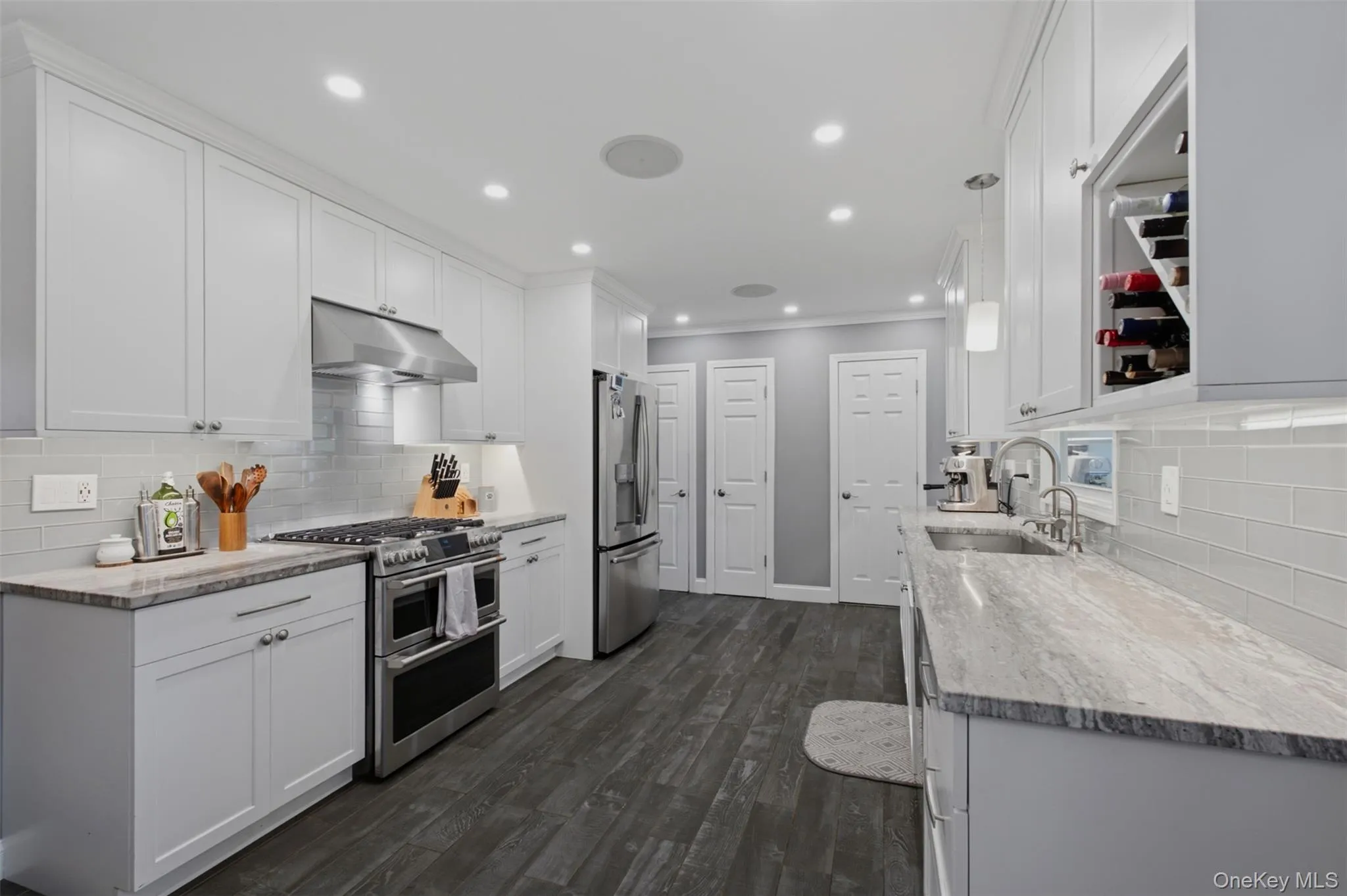 Sleek kitchen featuring white shaker cabinetry, stainless steel appliances, grey stone countertops, a subway tile backsplash, and wood-finish flooring Sleek kitchen featuring white shaker cabinetry, stainless steel appliances, grey stone countertops, a subway tile backsplash, and wood-finish flooring