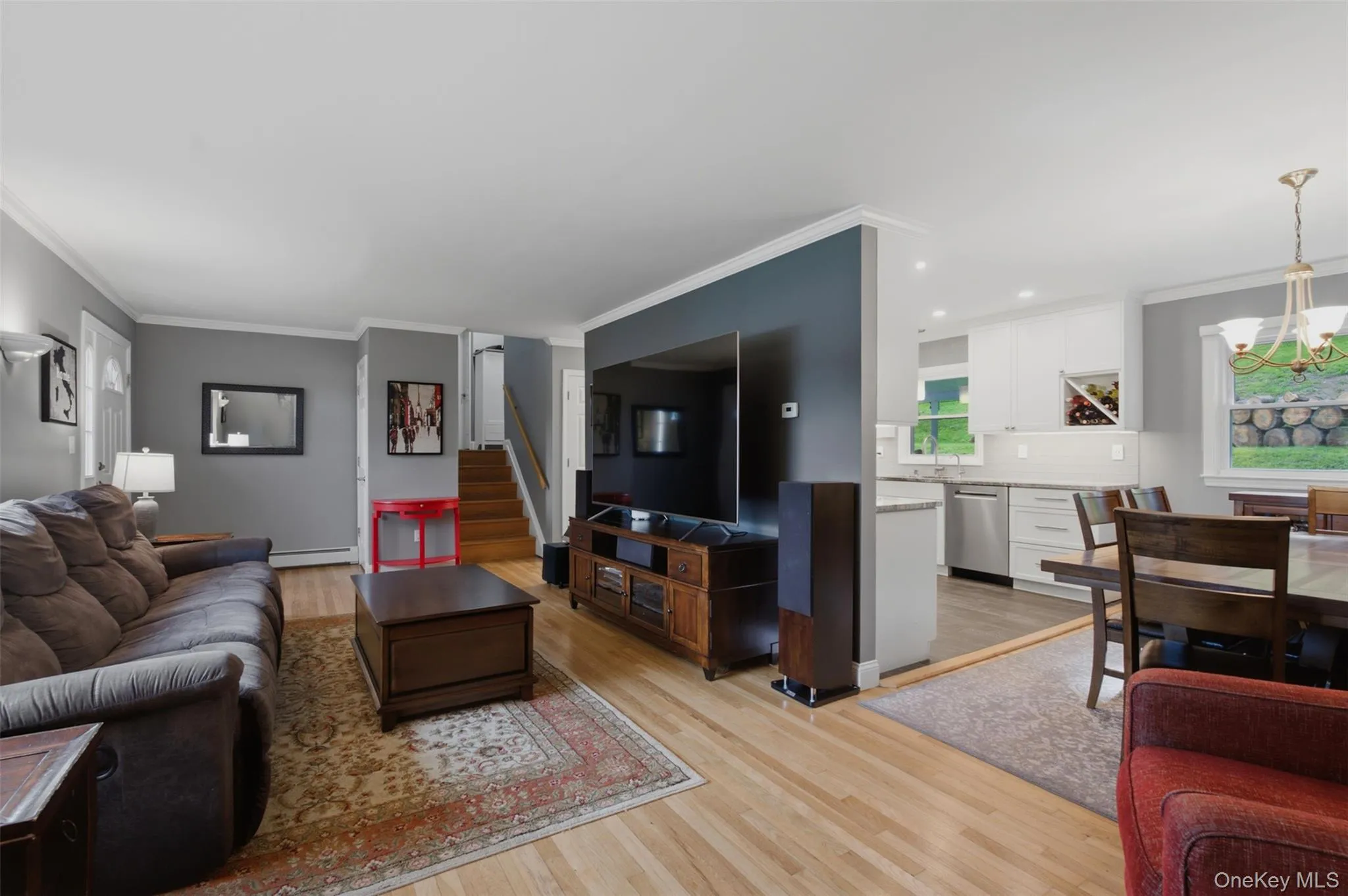 Open-concept living area featuring light wood-finish flooring, white crown molding, and a partial wall separating living and kitchen areas Open-concept living area featuring light wood-finish flooring, white crown molding, and a partial wall separating living and kitchen areas