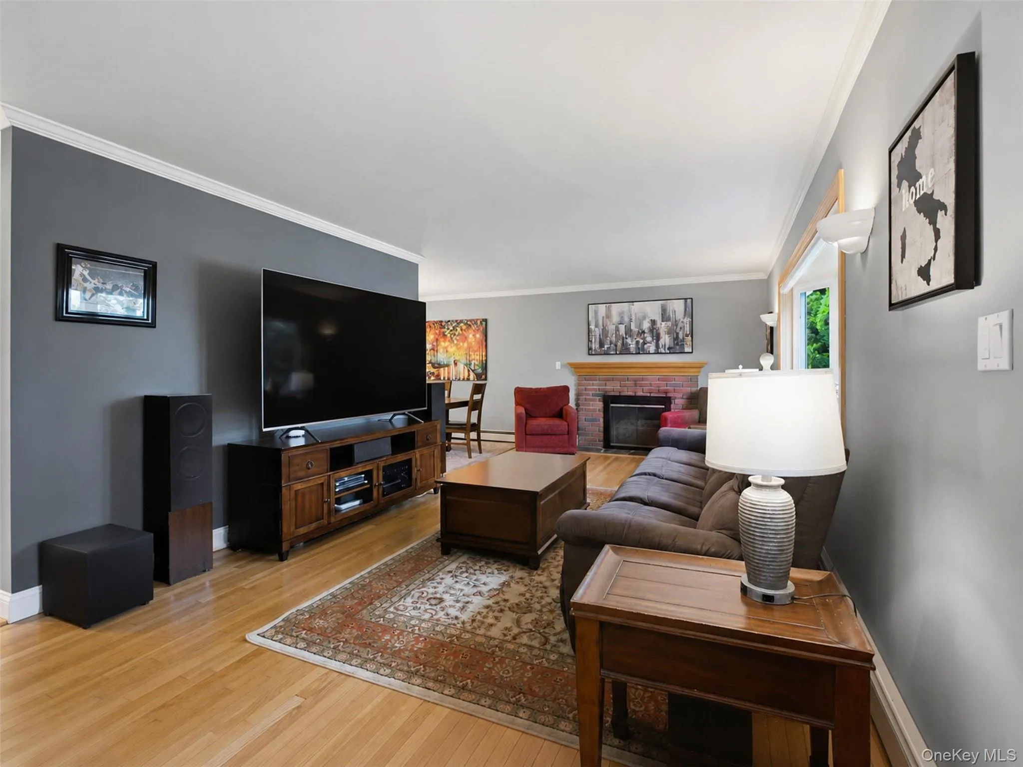 Living area featuring light wood-finish flooring and a red brick fireplace Living area featuring light wood-finish flooring and a red brick fireplace