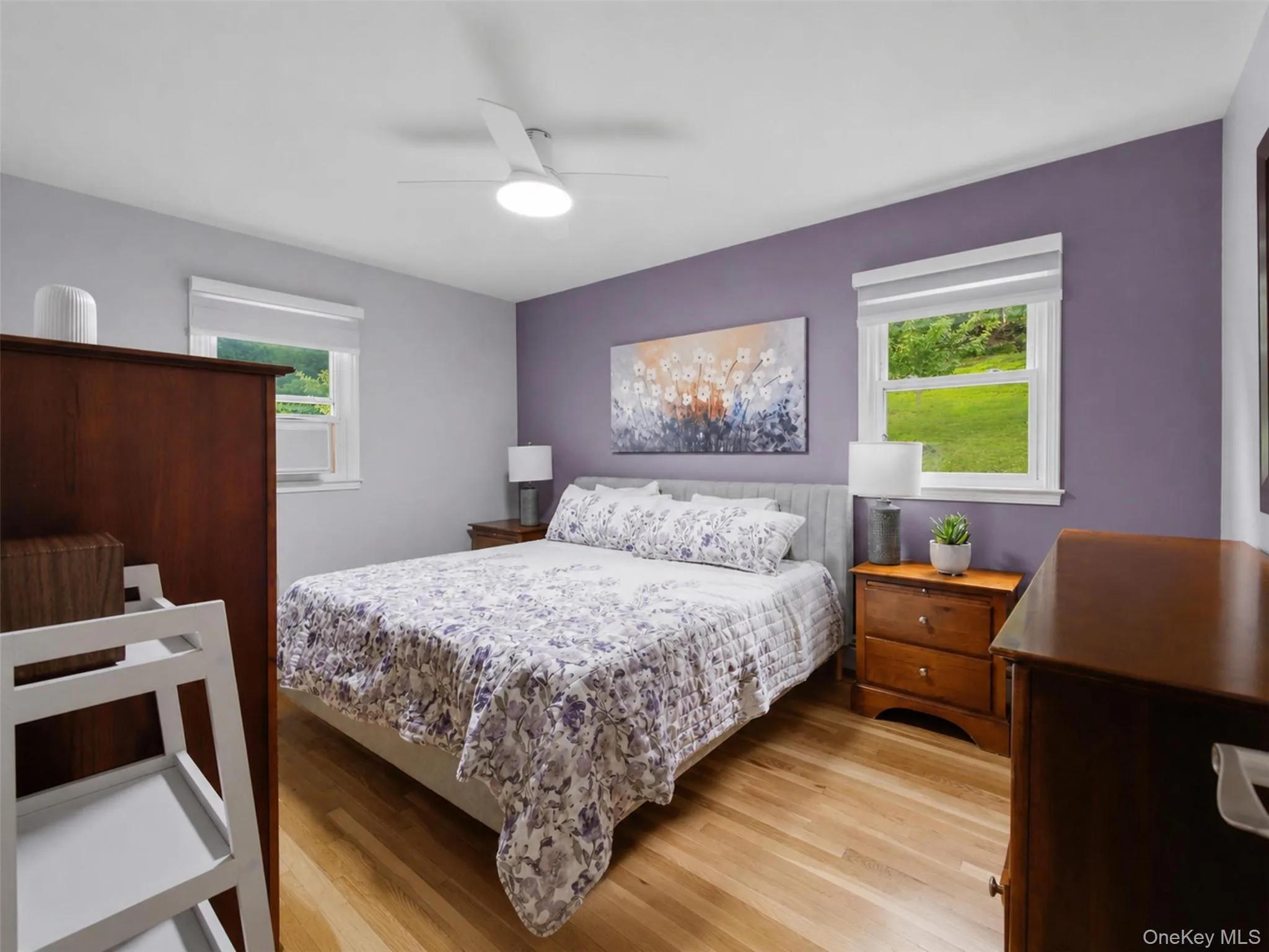 Bedroom featuring wood-finish flooring, a contemporary ceiling fan with integrated lighting, and two windows providing outdoor illumination Bedroom featuring wood-finish flooring, a contemporary ceiling fan with integrated lighting, and two windows providing outdoor illumination