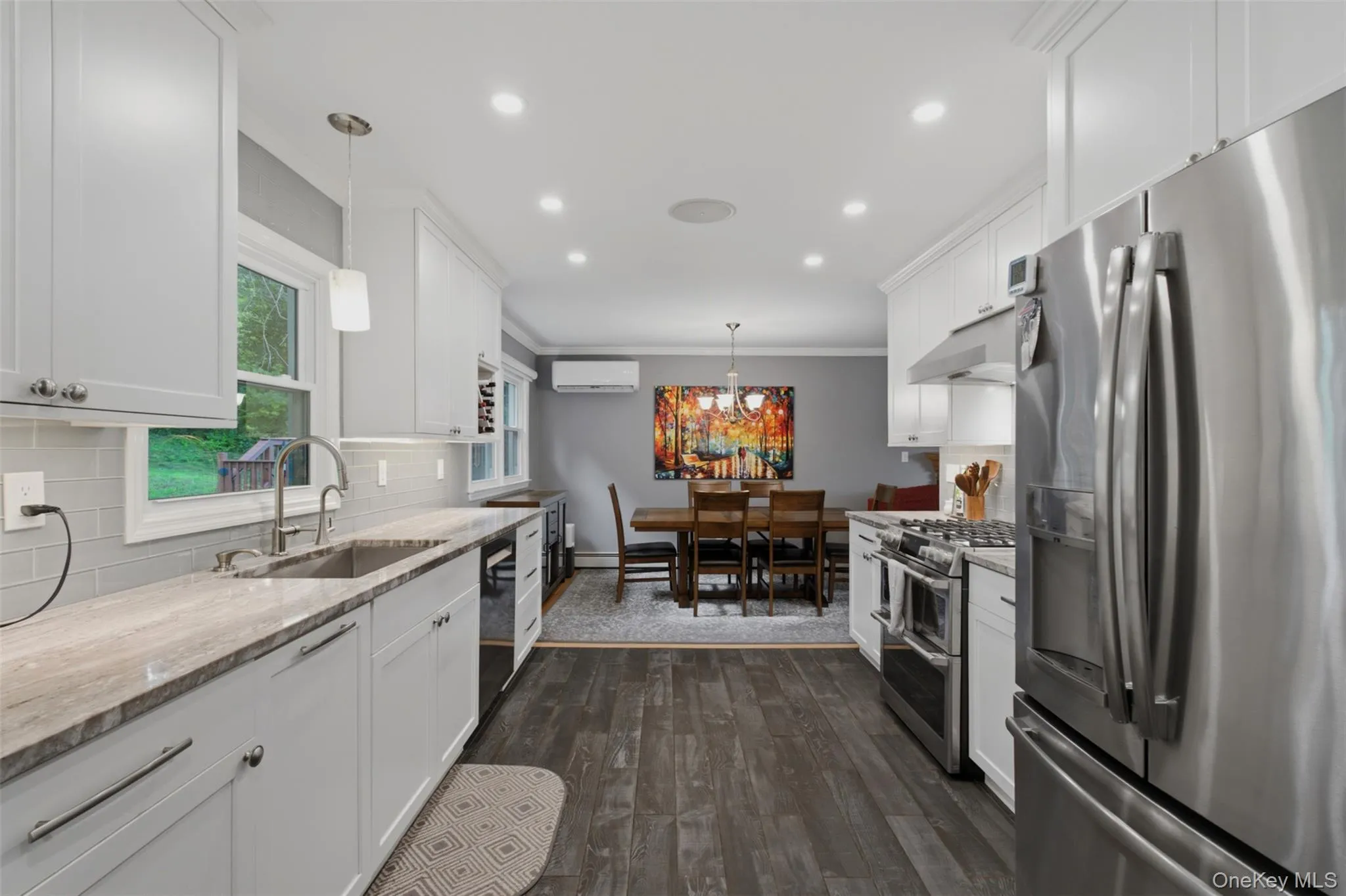 Modern kitchen featuring white shaker cabinetry, stainless steel appliances, wood-finish flooring, recessed lighting, and a subway tile backsplash Modern kitchen featuring white shaker cabinetry, stainless steel appliances, wood-finish flooring, recessed lighting, and a subway tile backsplash