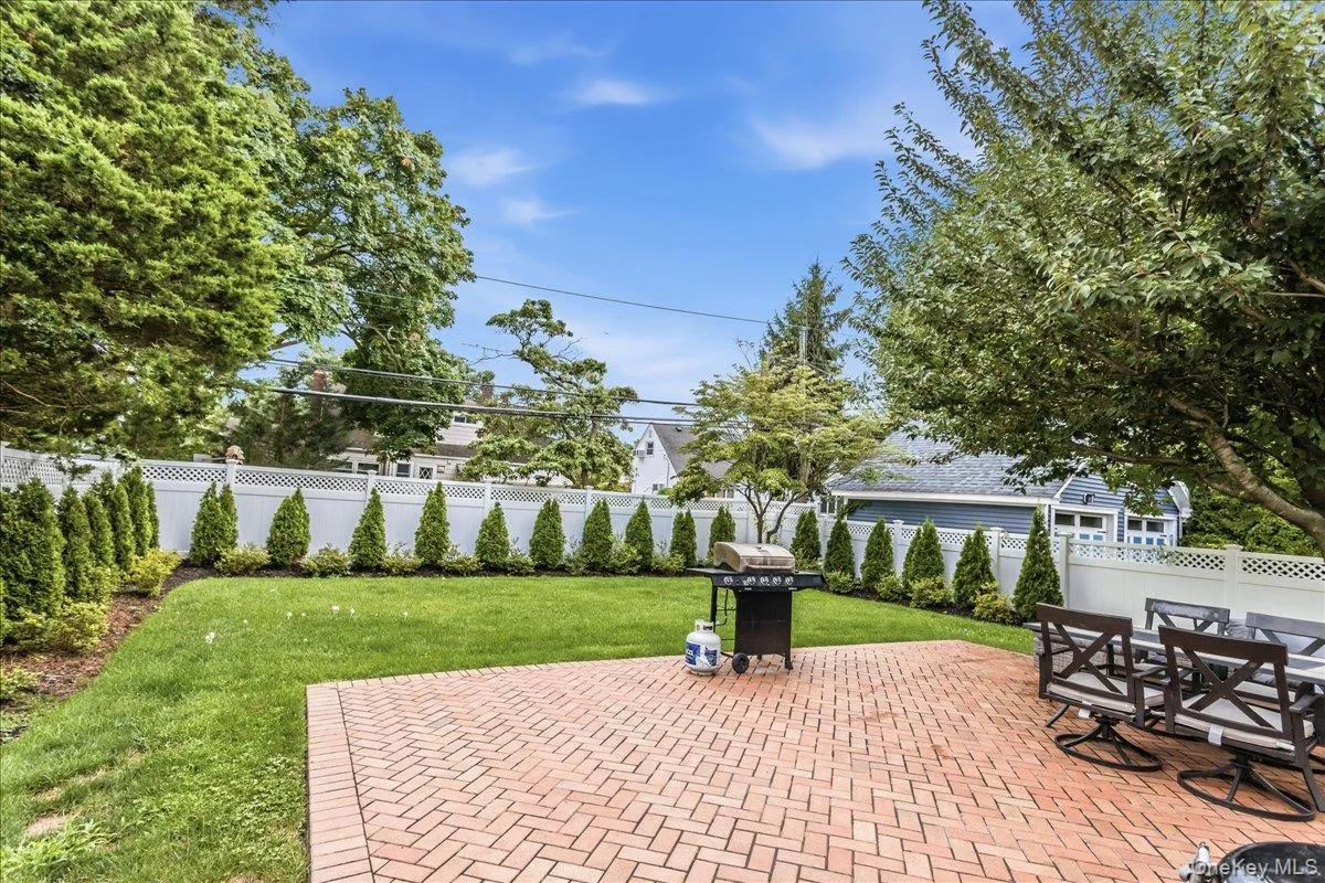 Expansive backyard featuring a brick paver patio, a manicured lawn, a white lattice fence, mature trees, and evergreen landscaping Expansive backyard featuring a brick paver patio, a manicured lawn, a white lattice fence, mature trees, and evergreen landscaping