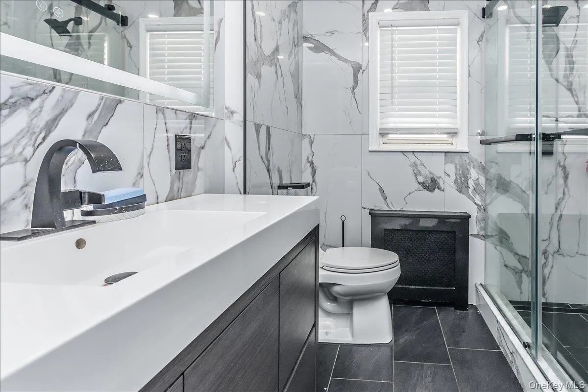 Spa-inspired primary bathroom featuring marble-look wall tile, dark tile flooring, and a floating vanity with an integrated rectangular sink Spa-inspired primary bathroom featuring marble-look wall tile, dark tile flooring, and a floating vanity with an integrated rectangular sink