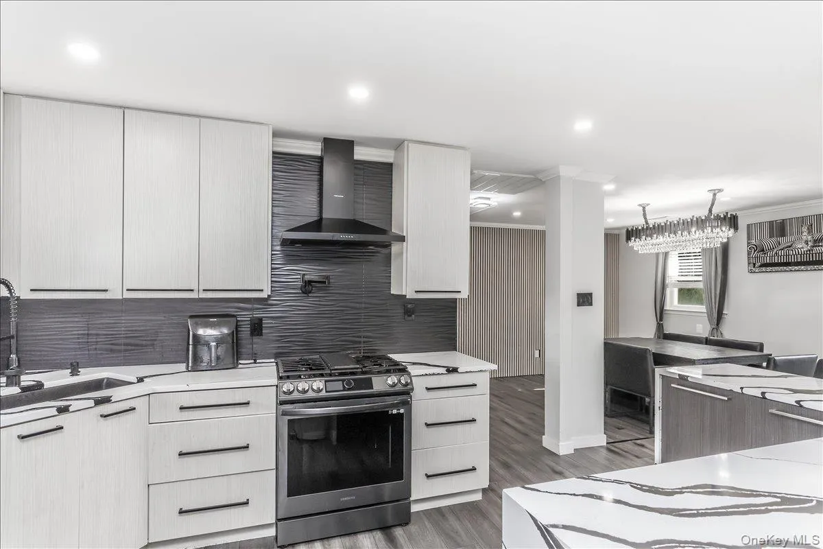 Modern kitchen featuring light wood-finish cabinetry, dark horizontal hardware, and a stainless steel gas range with a coordinating range hood Modern kitchen featuring light wood-finish cabinetry, dark horizontal hardware, and a stainless steel gas range with a coordinating range hood