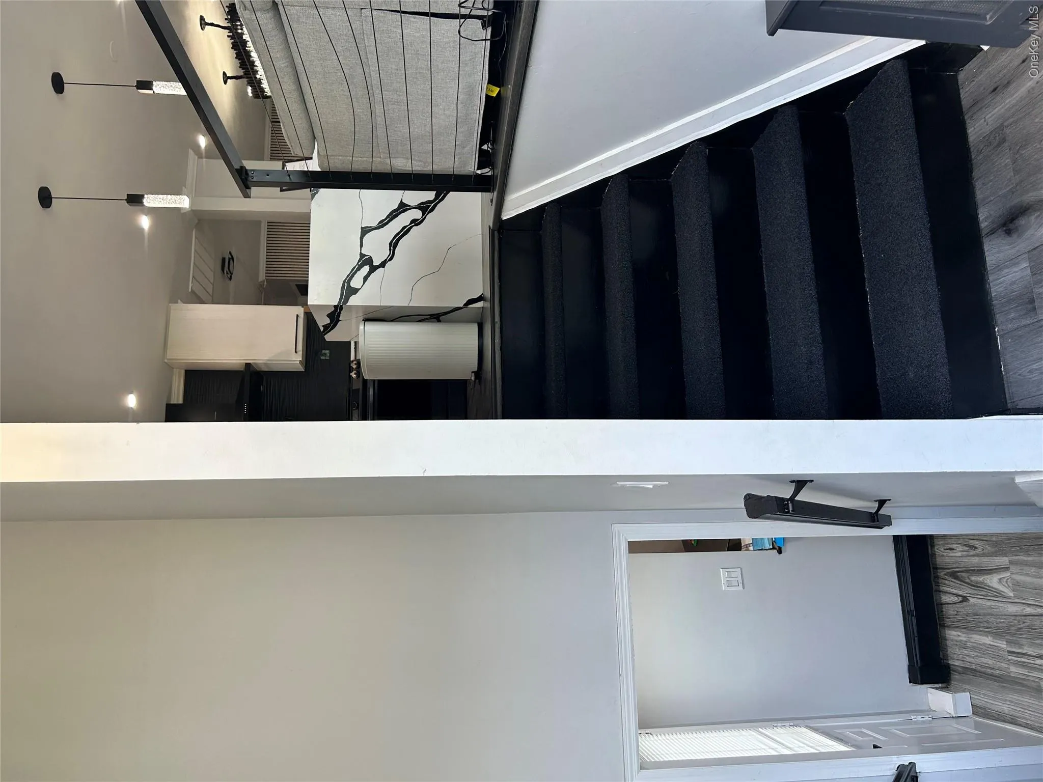Contrasting black staircase with a partial railing, wood-finish flooring, and a kitchen featuring white upper cabinetry and a dark range hood Contrasting black staircase with a partial railing, wood-finish flooring, and a kitchen featuring white upper cabinetry and a dark range hood