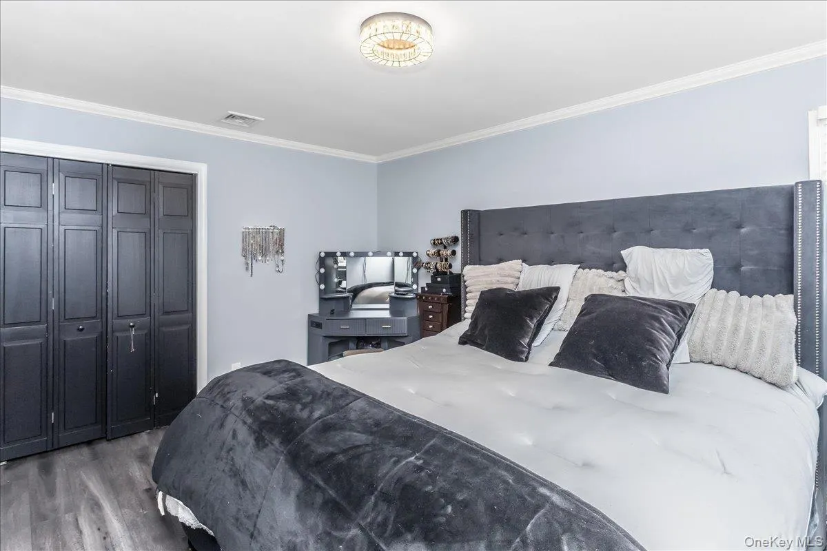 Bedroom featuring wood-finish flooring, crown molding, and a contemporary ceiling light fixture Bedroom featuring wood-finish flooring, crown molding, and a contemporary ceiling light fixture