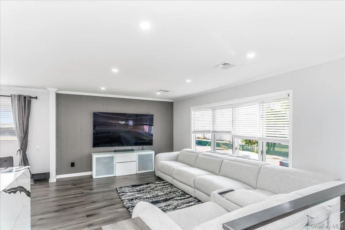 Spacious living area featuring wood-finish flooring, recessed lighting, and a prominent accent wall Spacious living area featuring wood-finish flooring, recessed lighting, and a prominent accent wall