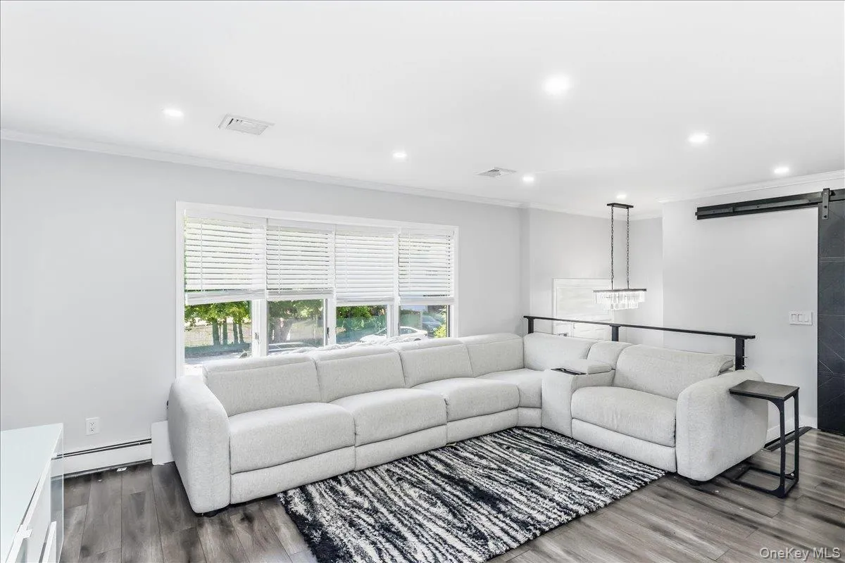 Living area featuring recessed lighting, a multi-window wall with blinds, dark wood-finish flooring, and a modern chandelier Living area featuring recessed lighting, a multi-window wall with blinds, dark wood-finish flooring, and a modern chandelier