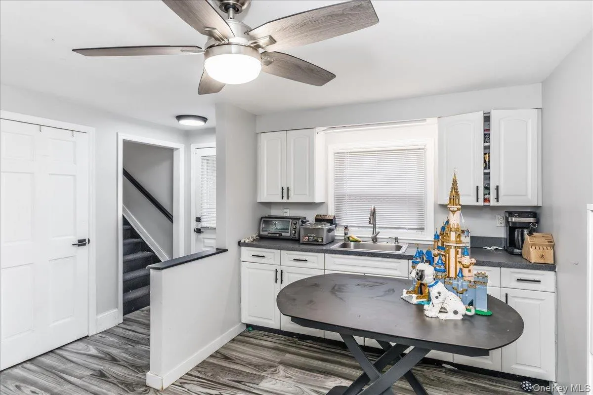 Modern kitchen area featuring white cabinetry, dark countertops, and wood-finish flooring Modern kitchen area featuring white cabinetry, dark countertops, and wood-finish flooring