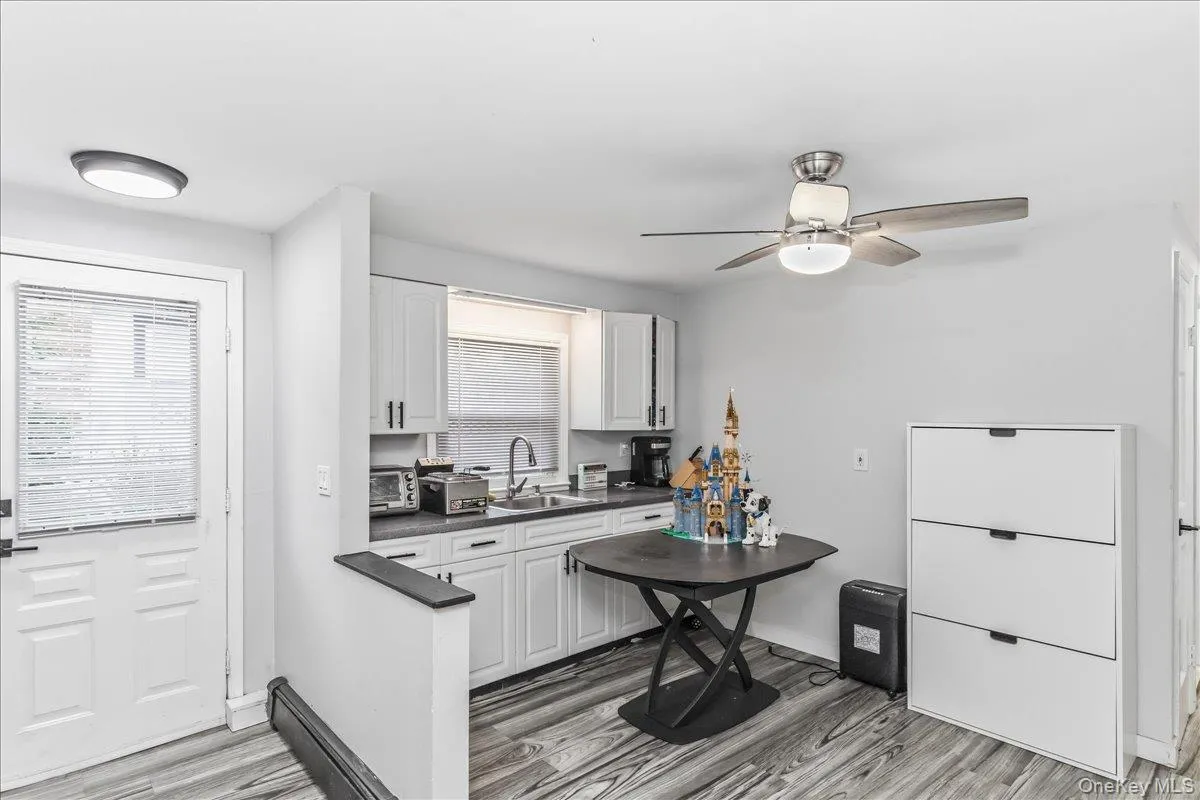 Contemporary kitchen featuring white cabinetry, dark countertops, a stainless steel sink with a gooseneck faucet, and wood-finish flooring Contemporary kitchen featuring white cabinetry, dark countertops, a stainless steel sink with a gooseneck faucet, and wood-finish flooring