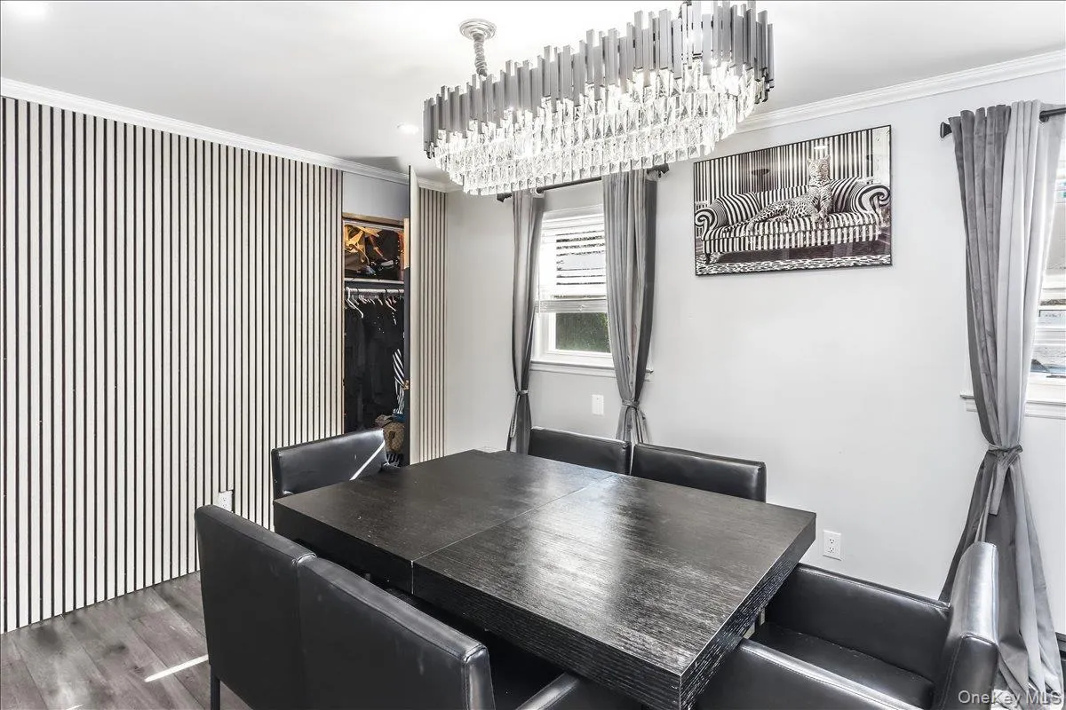 Dining area featuring a contemporary chandelier, wood-finish flooring, two windows, and a built-in closet with slatted panel doors Dining area featuring a contemporary chandelier, wood-finish flooring, two windows, and a built-in closet with slatted panel doors