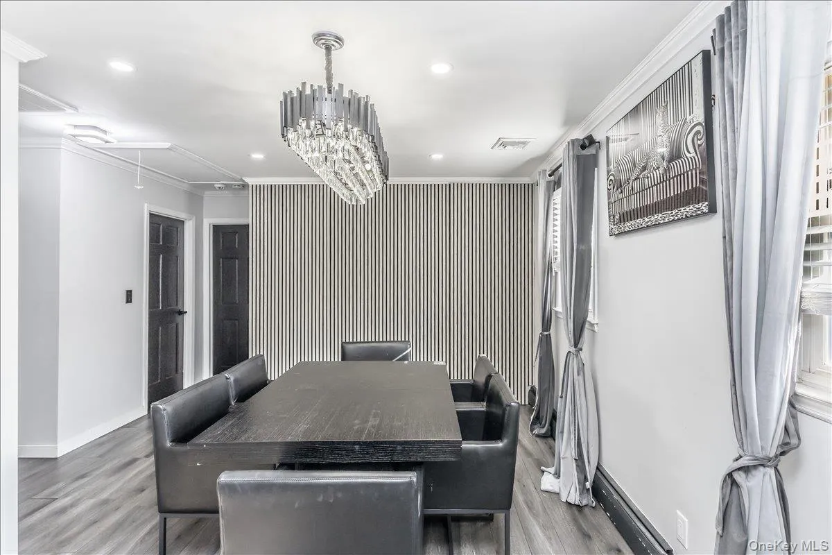 Dining space featuring wood-finish flooring, a contemporary crystal chandelier, a striped accent wall, and two paneled doors with dark finishes Dining space featuring wood-finish flooring, a contemporary crystal chandelier, a striped accent wall, and two paneled doors with dark finishes