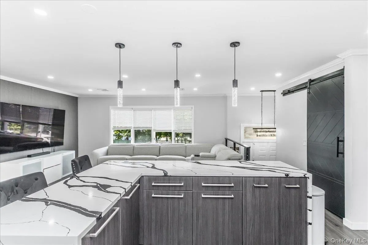 Kitchen island featuring a waterfall-edge countertop with prominent veining, wood-finish cabinetry, and three pendant lights Kitchen island featuring a waterfall-edge countertop with prominent veining, wood-finish cabinetry, and three pendant lights