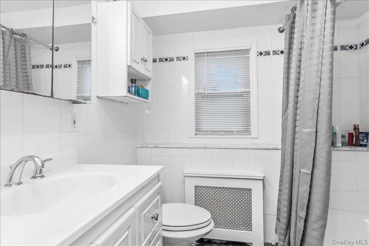 Bathroom featuring white tiled walls, a white vanity with integrated sink, and a chrome faucet Bathroom featuring white tiled walls, a white vanity with integrated sink, and a chrome faucet