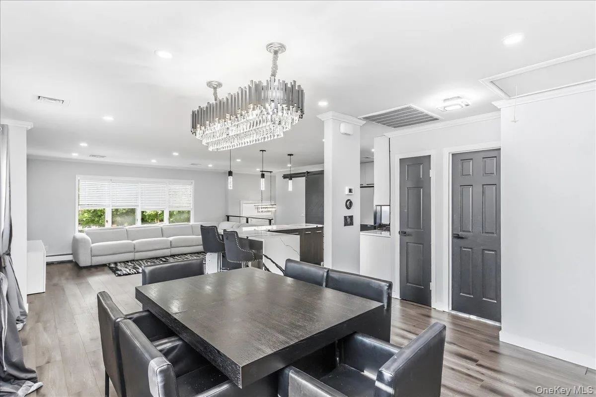 Open-concept interior featuring wood-finish flooring, a contemporary chandelier, recessed lighting, a kitchen island with seating, and dark panel doors Open-concept interior featuring wood-finish flooring, a contemporary chandelier, recessed lighting, a kitchen island with seating, and dark panel doors