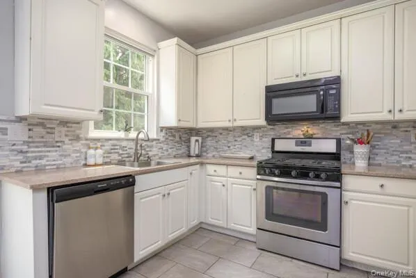 Kitchen with white shaker-style cabinetry, mosaic tile backsplash, stainless steel appliances, and a window above the sink Kitchen with white shaker-style cabinetry, mosaic tile backsplash, stainless steel appliances, and a window above the sink