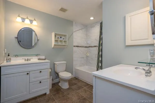 Bathroom featuring a white vanity with an integrated sink, a second white vanity with a white countertop and drop-in sink, a built-in tub with tile surround, and brown tile flooring Bathroom featuring a white vanity with an integrated sink, a second white vanity with a white countertop and drop-in sink, a built-in tub with tile surround, and brown tile flooring
