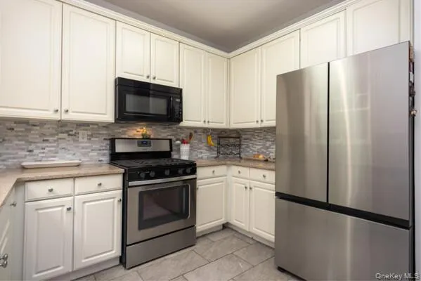 Kitchen featuring white cabinetry, light-toned countertops, tile backsplash, and stainless steel appliances Kitchen featuring white cabinetry, light-toned countertops, tile backsplash, and stainless steel appliances