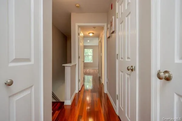 Hallway featuring warm-toned wood-finish flooring, white paneled doors, and neutral wall paint Hallway featuring warm-toned wood-finish flooring, white paneled doors, and neutral wall paint