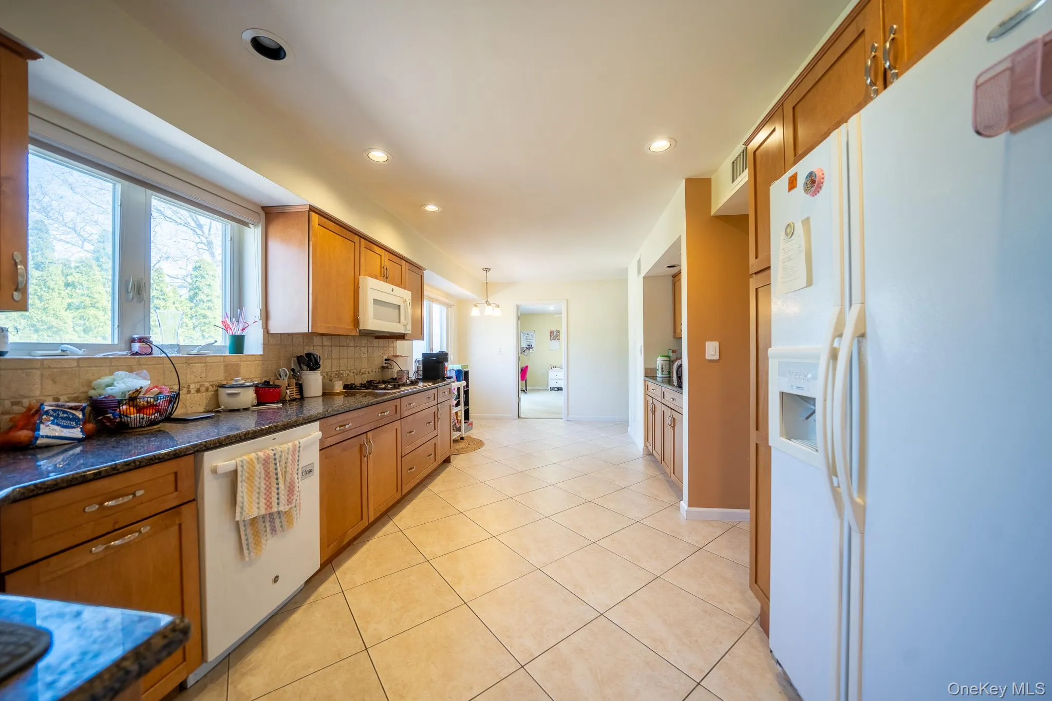Kitchen with tasteful backsplash, brown cabinetry, light tile patterned flooring, white appliances, and recessed lighting Kitchen with tasteful backsplash, brown cabinetry, light tile patterned flooring, white appliances, and recessed lighting