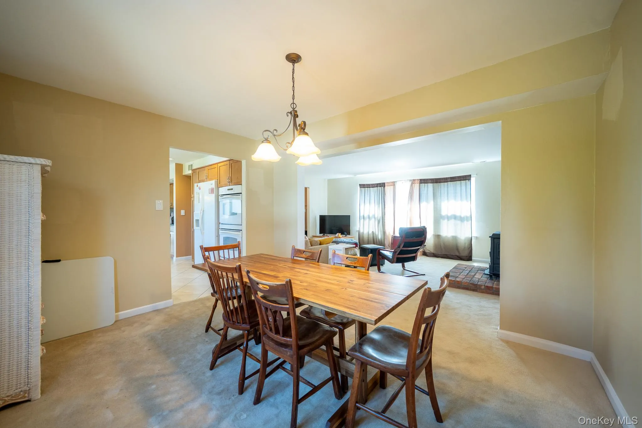 Dining room with baseboards, a wood stove, light colored carpet, and a notable chandelier Dining room with baseboards, a wood stove, light colored carpet, and a notable chandelier